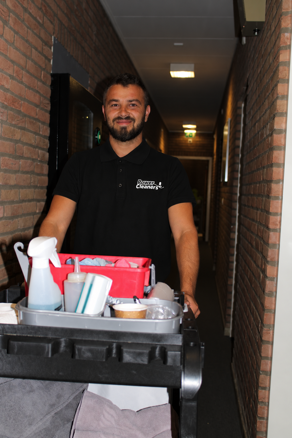 PowerCleaners medewerker met schoonmaakmaterialen in een gang